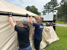 Two members of an incident management assistance team set up a tent shelter.