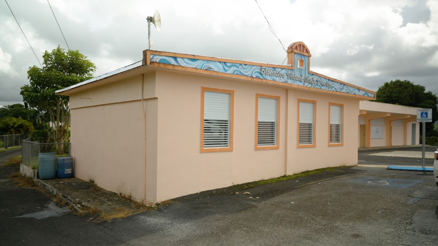 Light pink one story building with four white windows on front. View of a handicap parking.