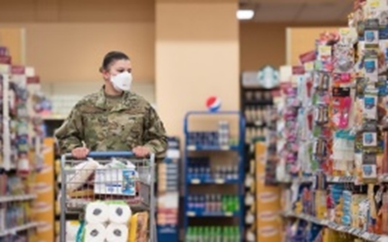 Service member wearing face mask pushing a shopping cart in a grocery store aisle