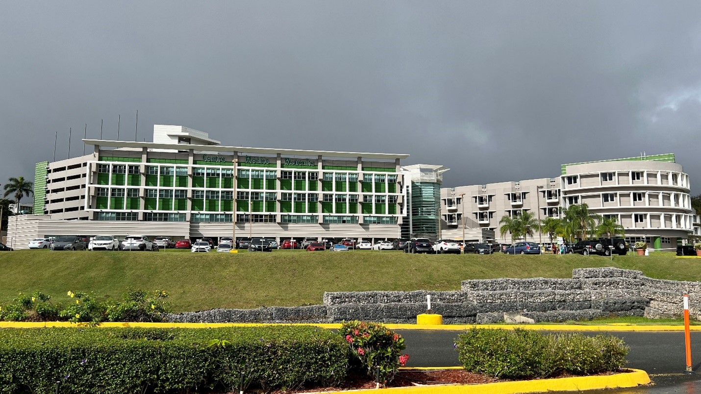 View of the Mennonite Ganeral Hospital buildings. At the right, three strory building with big glass windows. At the right, three story grey building with small  square windows.