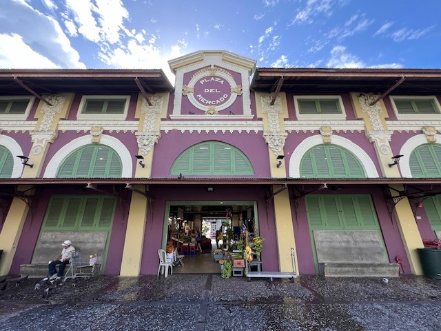 Entrada principal de la Plaza del Mercado de Santurce. Edificio es color violeta y amarillo con puertas y ventanas verdes.