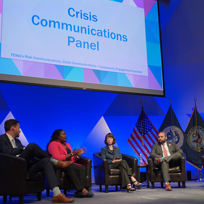 A picture of presenters on stage at the OEA Summit, under a slide that reads "Crisis Communications Panel"