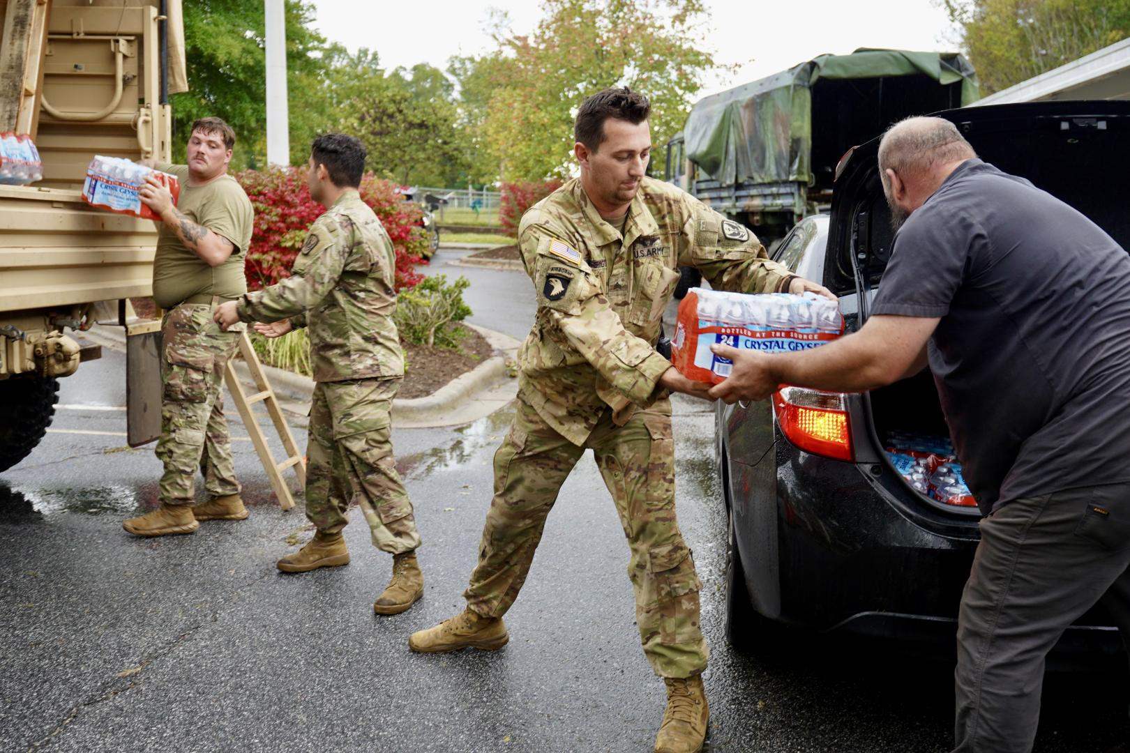 Members of the North Carolina Army National Guard work alongside volunteers at William W. Estes Elementary School to load meals and water for disaster survivors. 