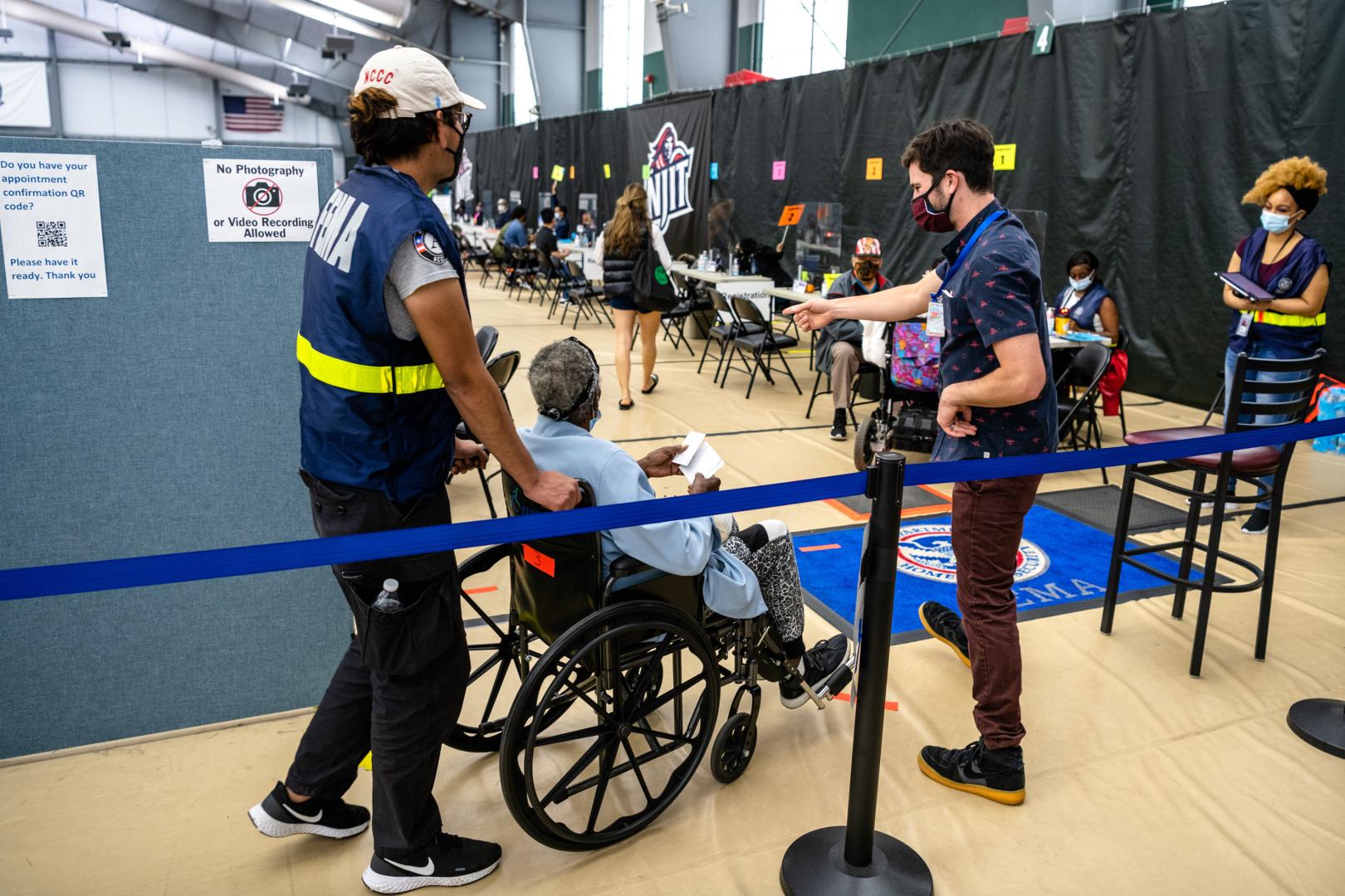 Man in FEMA vest pushes woman in wheelchair into Disaster Recovery Center.