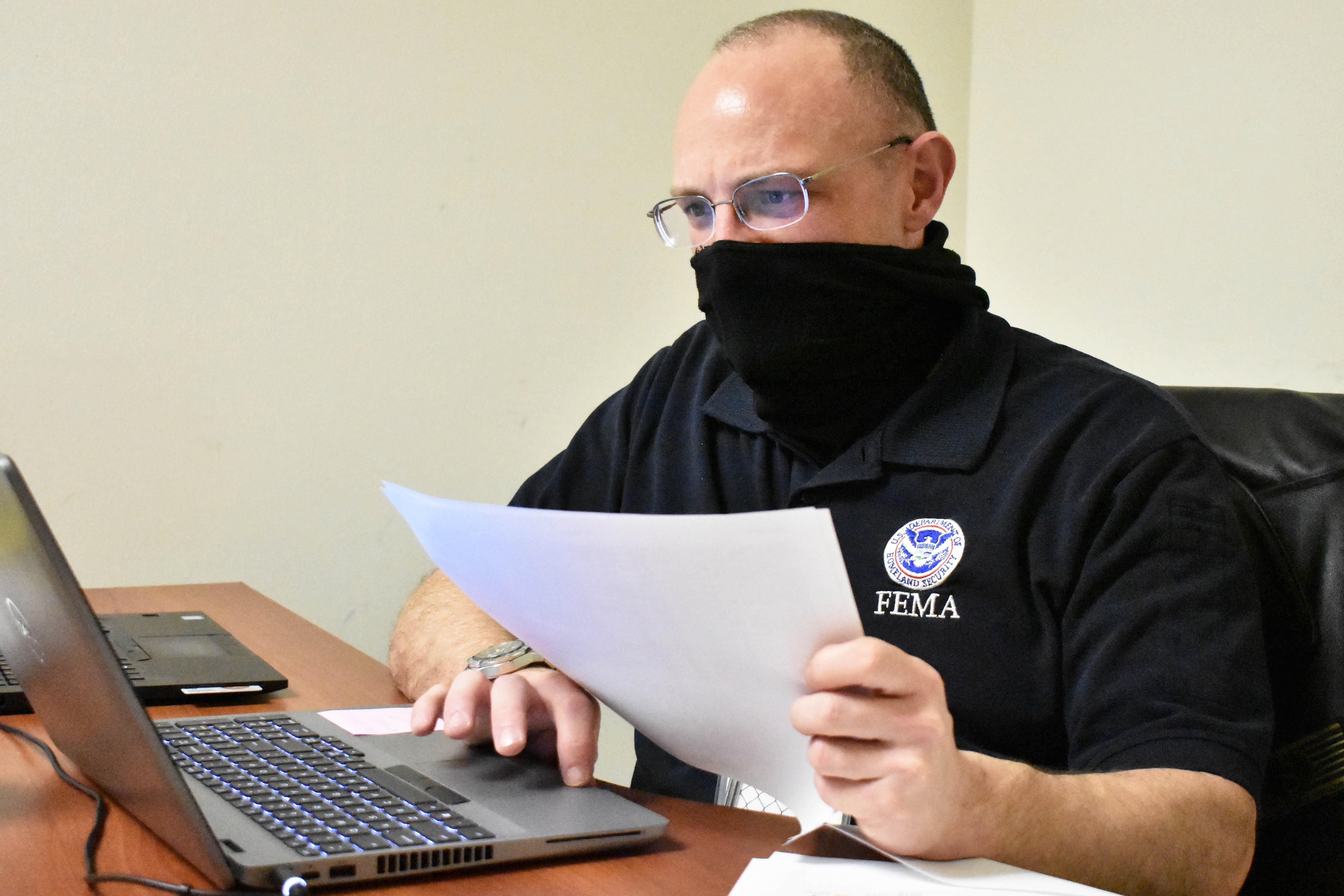 A man working on his laptop with papers in his left hand. 