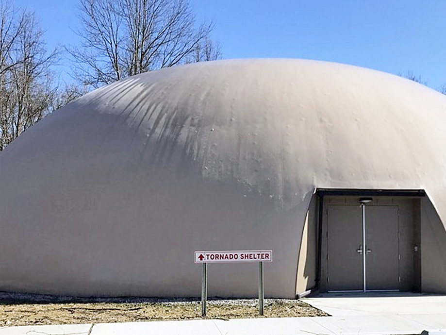 A picture showing a dome storm shelter. The sign in front of the shelter reads "tornado shelter".