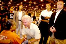 President Bill Clinton greets a wheelchair-bound evacuee in the Reliant Center at the Houston Astrodome. He and President George Walker Bush were at the Astrodome to announce a new relief fund. In the background, holding his jacket is Senator Barack Obama. 