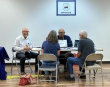 FEMA staff sitting at tables speaking with a survivor at a Disaster Recovery Center. Sign on wall says "Mitigation"