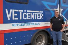 A person standing next to a blue Department of Veterans Affairs Vet Center truck.