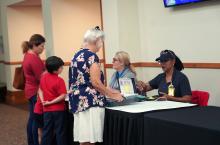 Two women FEMA specialist sitting at table with two women standing with two small children in the middle of them.