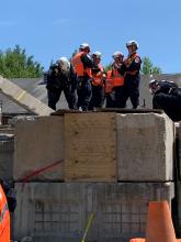 Three men stand next to cement wall holding large objects.