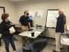 2 males and a female in a room discussing plans and writing them on a white board